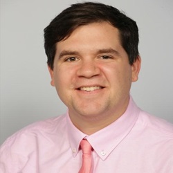 A SUNY New Paltz alumni wearing a pink shirt and tie poses for a photo